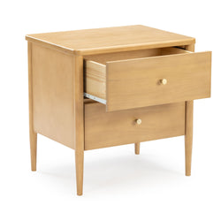 Mid-century modern light wood bedside nightstand with open top drawer, round brass knobs and tapered legs on white background