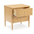 Mid-century modern light wood bedside nightstand with open top drawer, round brass knobs and tapered legs on white background