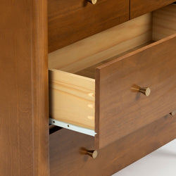 Close-up of solid wood dresser drawer showing dovetail joints, light maple interior, brass knob and metal drawer slide