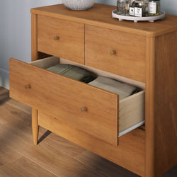 Mid-century modern solid wood dresser with open lower drawer revealing neatly folded clothes, teak-finish chest of drawers with brass knobs on hardwood floor
