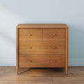 Mid-century modern oak four-drawer dresser with brass knobs, natural wood finish on hardwood floor against a light blue wall
