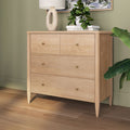 Light wood mid-century modern four-drawer dresser with brass knobs in a styled green bedroom setting with plants