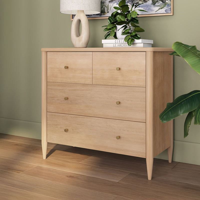 Light wood mid-century modern four-drawer dresser with brass knobs in a styled green bedroom setting with plants