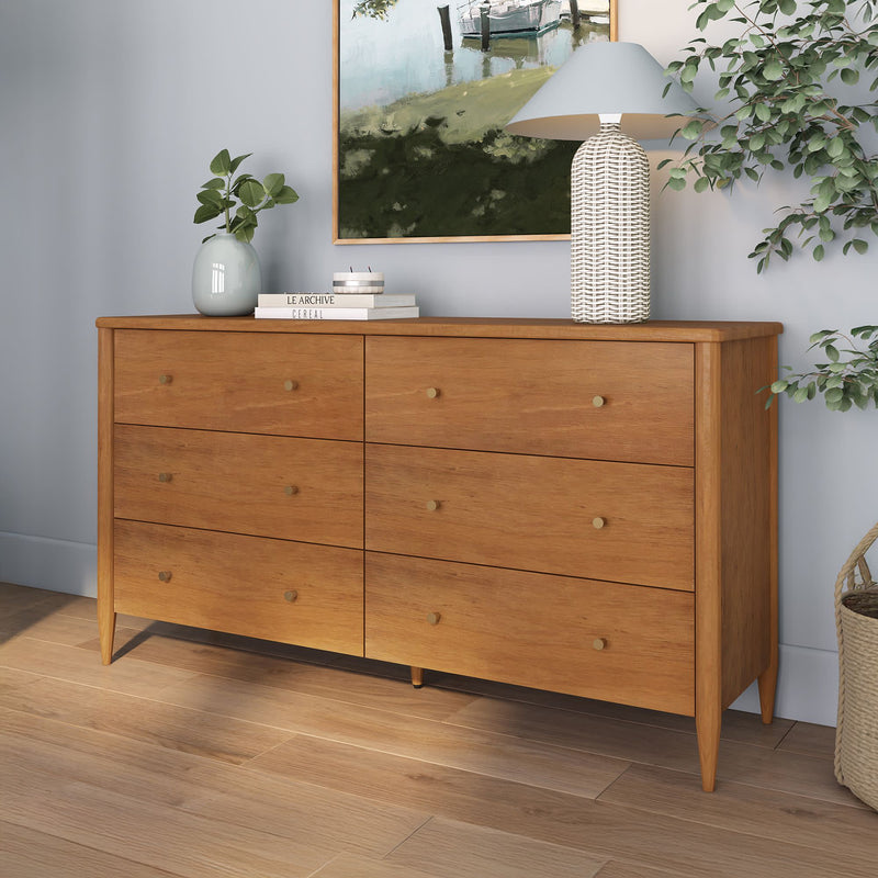 Mid-century modern six-drawer oak dresser with natural wood finish, styled bedroom storage with lamp, plant and framed art