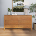 Mid-century six-drawer light oak dresser with brass knobs, styled with wicker lamp, potted plant and coastal painting