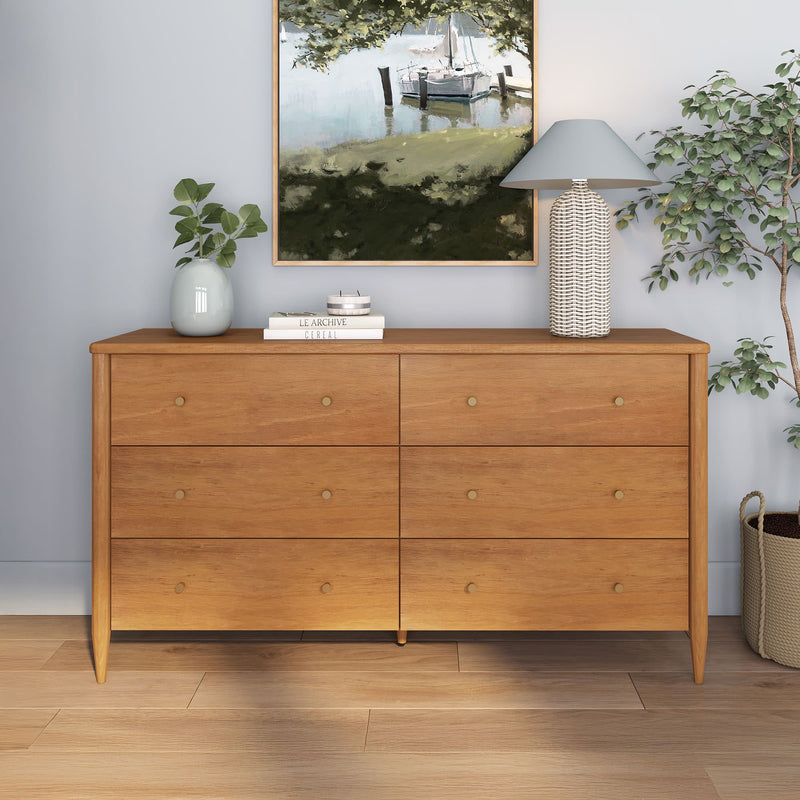 Mid-century six-drawer light oak dresser with brass knobs, styled with wicker lamp, potted plant and coastal painting