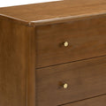 Close-up of warm walnut-tone solid wood dresser with rounded top edge and gold brass drawer knobs, mid-century modern style