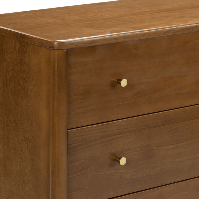 Close-up of warm walnut-tone solid wood dresser with rounded top edge and gold brass drawer knobs, mid-century modern style