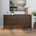 Mid-century modern dark wood six-drawer dresser styled with rattan table lamp, sailboat wall art, small potted plants on hardwood floor