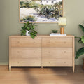 Light natural wood six-drawer dresser in a modern bedroom styled with a potted plant, table lamp, coastal wall art and hardwood floors