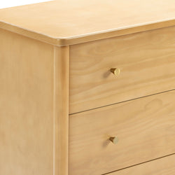 Close-up of light maple wood dresser corner with smooth finish and round brass drawer knob