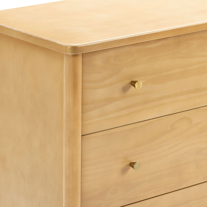 Close-up of light maple wood dresser corner with smooth finish and round brass drawer knob
