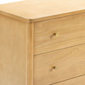 Close-up of light maple wood dresser corner with smooth finish and round brass drawer knob