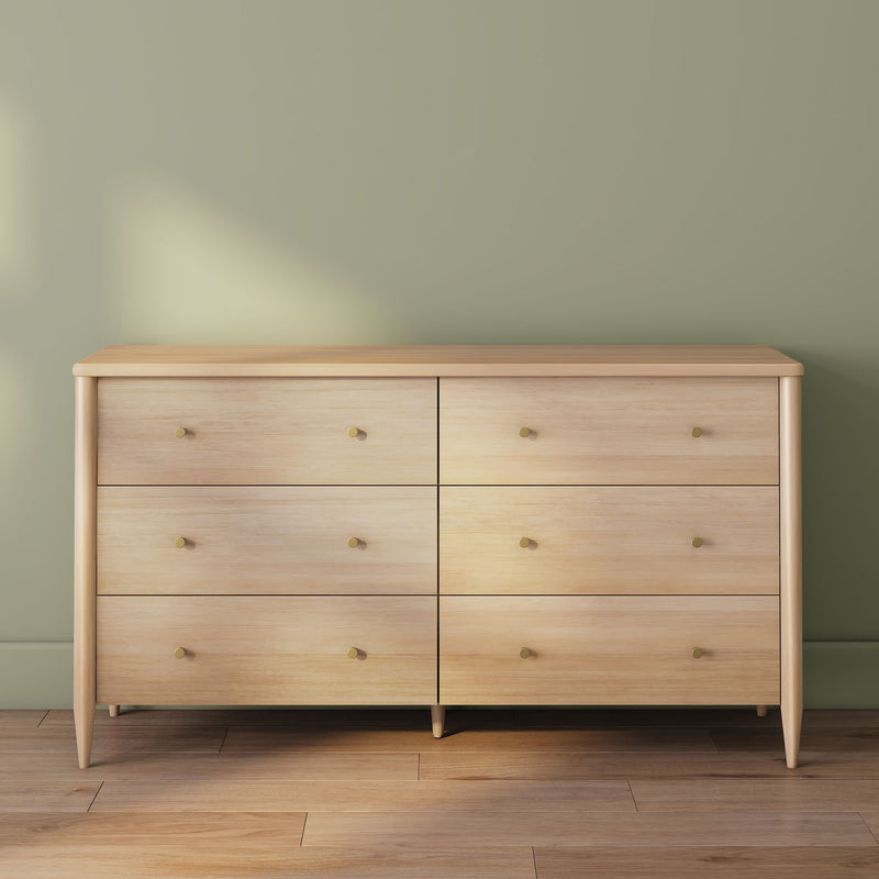 Light wood six-drawer dresser with brass knobs on hardwood floor against sage green wall, modern mid-century bedroom storage