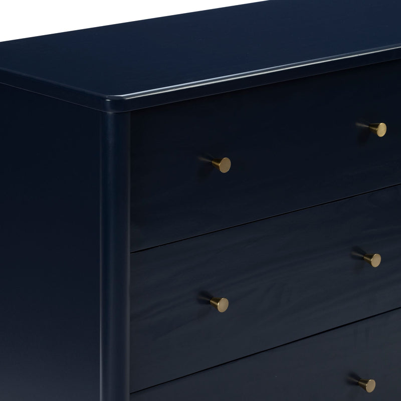 Close-up of navy blue lacquered dresser drawers with round brass knobs, modern bedroom storage cabinet