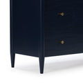Close-up of navy blue wooden nightstand with brass drawer knobs and tapered mid-century style legs