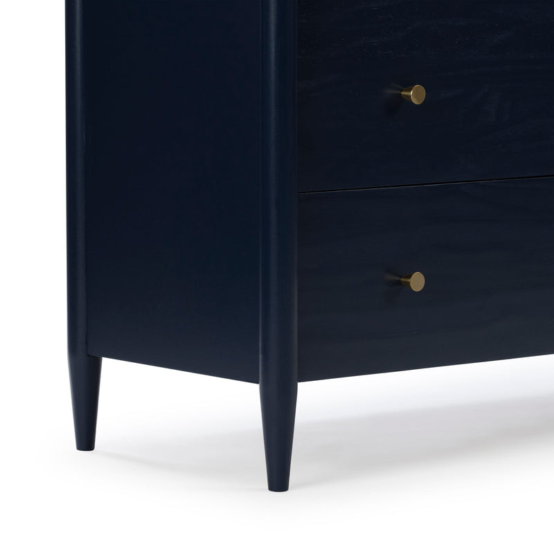 Close-up of navy blue wooden nightstand with brass drawer knobs and tapered mid-century style legs