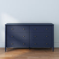 Navy blue six-drawer dresser with brass knobs on hardwood floor in minimalist modern bedroom interior