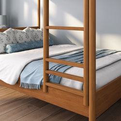 Light wood four-poster bed with white duvet, blue throw blanket and patterned lumbar pillows on hardwood floor