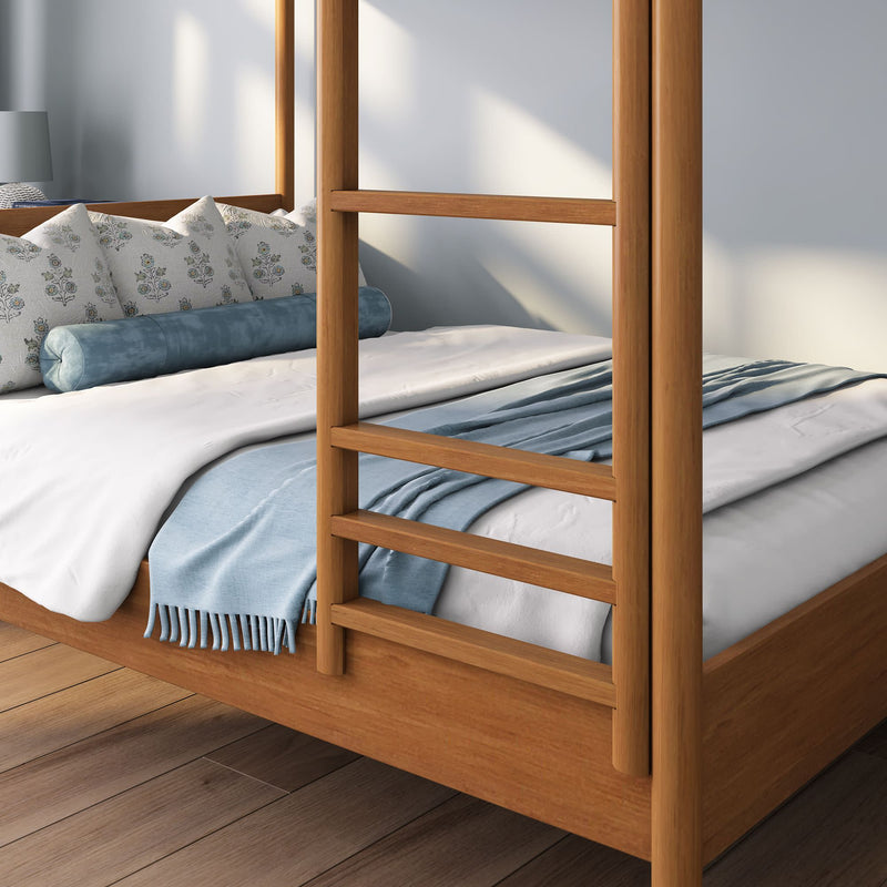 Light wood four-poster bed with white duvet, blue throw blanket and patterned lumbar pillows on hardwood floor