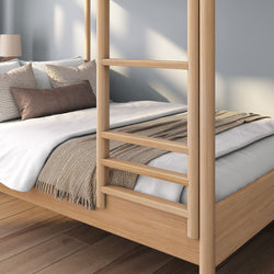 Modern solid wood four-poster platform bed with neutral white bedding, beige knit throw and decorative pillows on hardwood floor in minimalist master bedroom