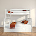 White wooden bunk bed with ladder and under-trundle drawer in a modern kids' bedroom, white bedding with rust-orange throws and pillows, neutral beige walls and hardwood floor bathed in natural light.