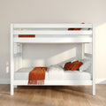 White wooden bunk bed with orange throw and pillows on hardwood floor in minimalist Scandinavian children's bedroom