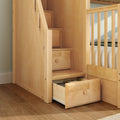 Natural maple built-in storage stairs with pull-out drawers on a kids loft bed beside crib railing — space-saving nursery furniture