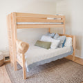 Light natural wood bunk bed in a bright neutral kids' bedroom with striped bedding, blue and green pillows, straw hat and beige textured rug