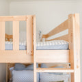 Close-up of a light maple wooden bunk bed showing safety rails and ladder with blue patterned bedding in a minimalist nursery