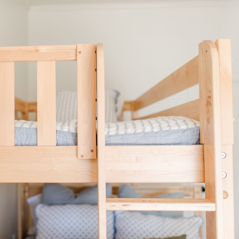 Close-up of a light maple wooden bunk bed showing safety rails and ladder with blue patterned bedding in a minimalist nursery