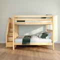 Natural maple wooden bunk bed with staircase storage, green pillows and throw on white mattress against pale gray wall in modern kids' bedroom
