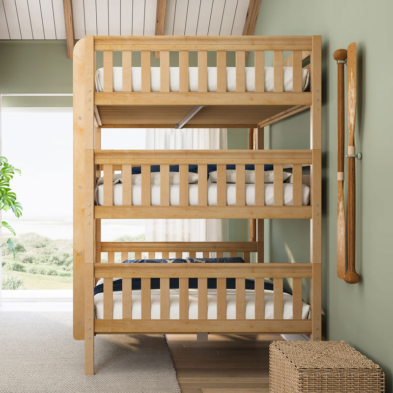 Solid wood triple bunk bed with white linens and navy accents in a light-filled coastal kids' bedroom with green walls, mounted wooden oars and a beach view
