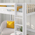 White wooden loft bed with ladder and natural wood slats above a cozy gray armchair with mustard yellow pillow and patterned blue bedding