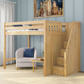 Light wood loft bed with staircase and built-in storage drawers above a cozy armchair reading nook with round side table and blue paneled wall