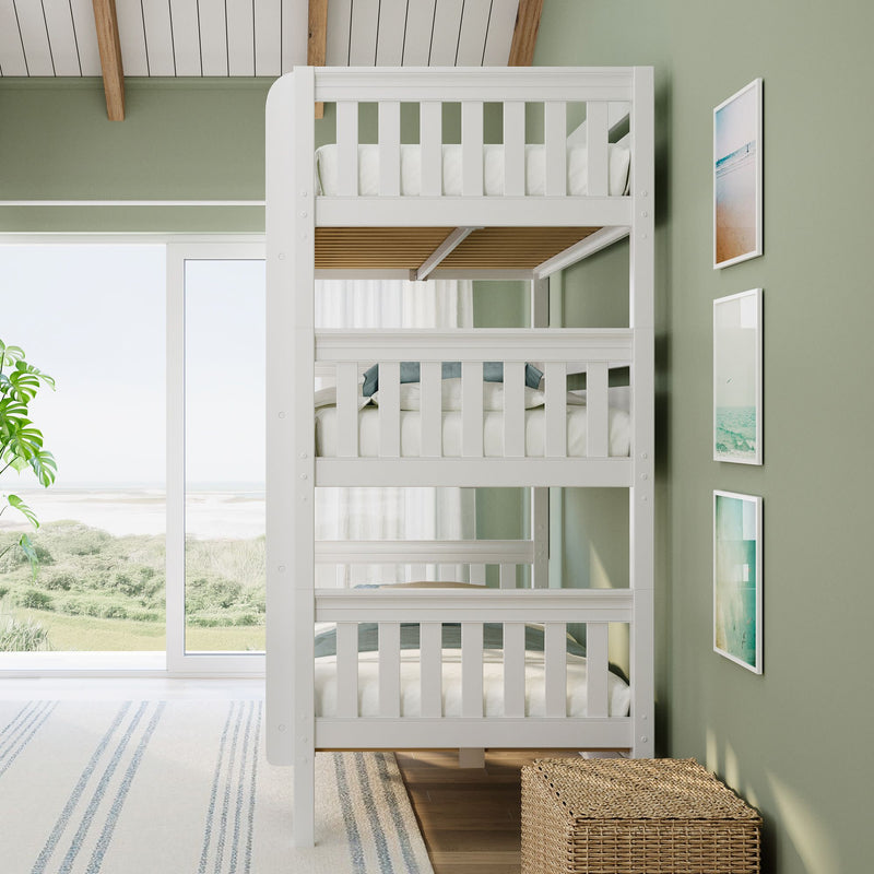 White triple bunk bed in sunlit coastal bedroom with sage green accent wall, wicker storage basket, framed beach prints and ocean view