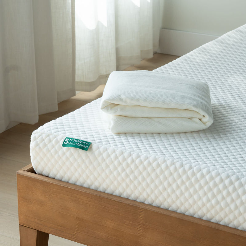 Memory foam mattress with folded white bedding on a wooden bed frame in a sunlit room.