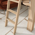 Close-up of a light wood ladder against a wooden loft platform on a neutral geometric area rug, next to a rust-colored velvet accent chair and round light wood side table — modern Scandinavian living room interior design