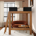 Modern wooden loft bed over rust-orange loveseat and round coffee table in bright loft apartment with exposed brick wall and large industrial window