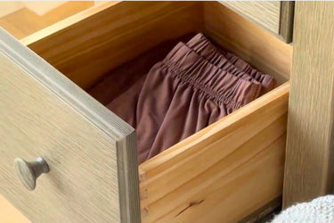 Open wooden dresser drawer with neatly folded mauve elastic-waist lounge shorts.