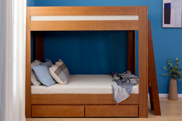 Modern wooden twin-over-twin bunk bed with ladder and under-bed storage drawers in a blue bedroom, lower bunk styled with pillows and a throw blanket.