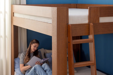Solid wood bunk bed with ladder in blue bedroom, lower bunk cozy reading nook with a young woman reading a book