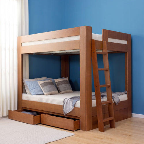 Solid wooden bunk bed with ladder and pull-out storage drawers in a modern bedroom with blue accent wall, made lower bed with pillows and throw