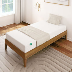 Single memory foam mattress on a wooden bed frame in a bright bedroom with hardwood floors.