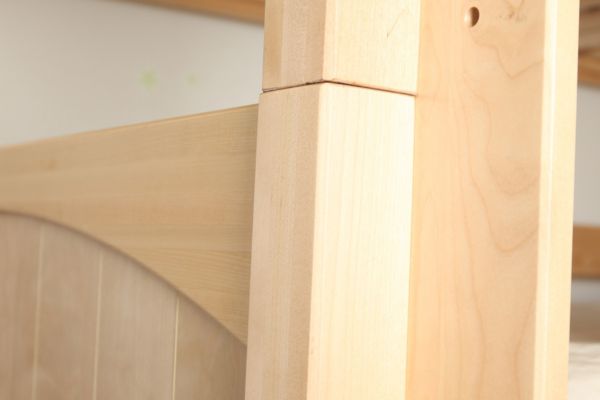 Close-up of a wooden bed frame corner with a neutral background.