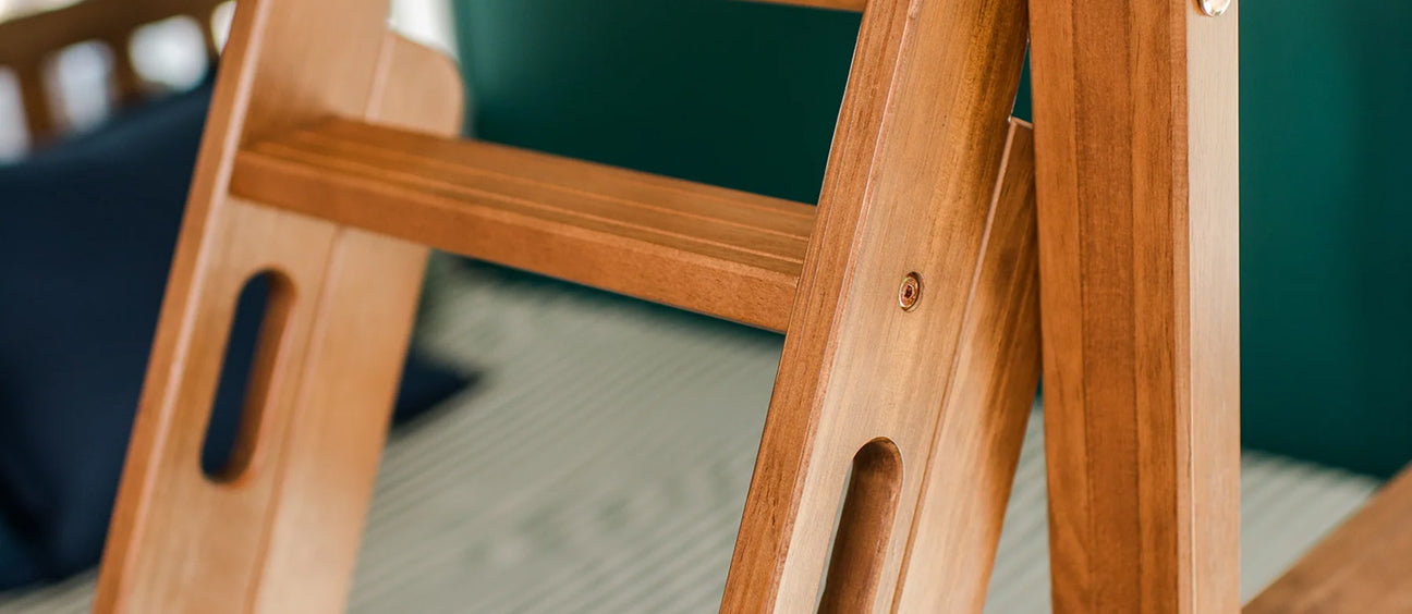 Close-up of solid wooden step ladder with smooth finish and rounded cutout handles leaning against a bed frame in a modern bedroom