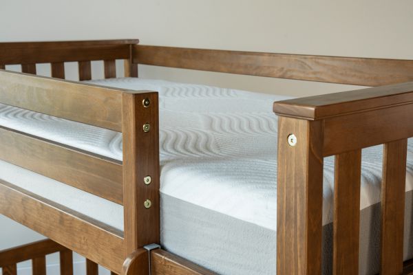 Wooden crib with a white mattress against a plain wall.