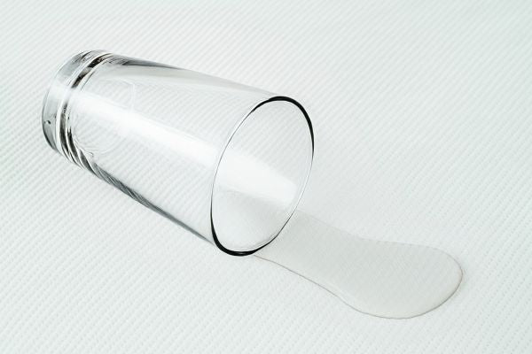 Clear tipped drinking glass spilling water onto white textured surface, minimalist still life.