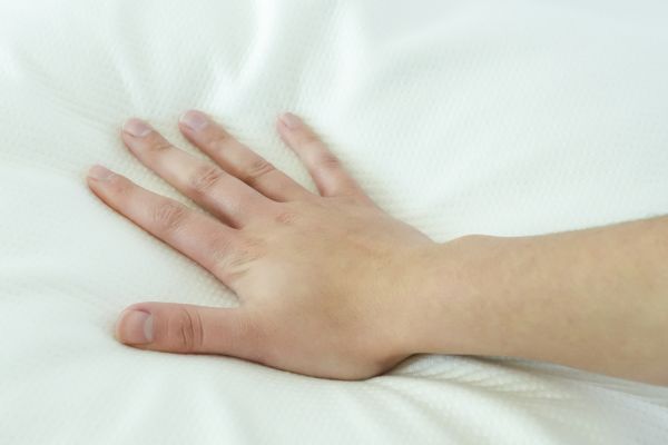 Hand pressing into white memory foam mattress to show pressure-relieving contouring and comfort.