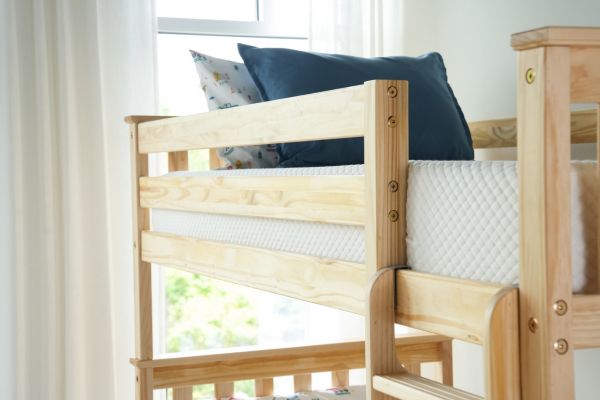 Wooden crib with white mattress and blue pillows in a bright room.